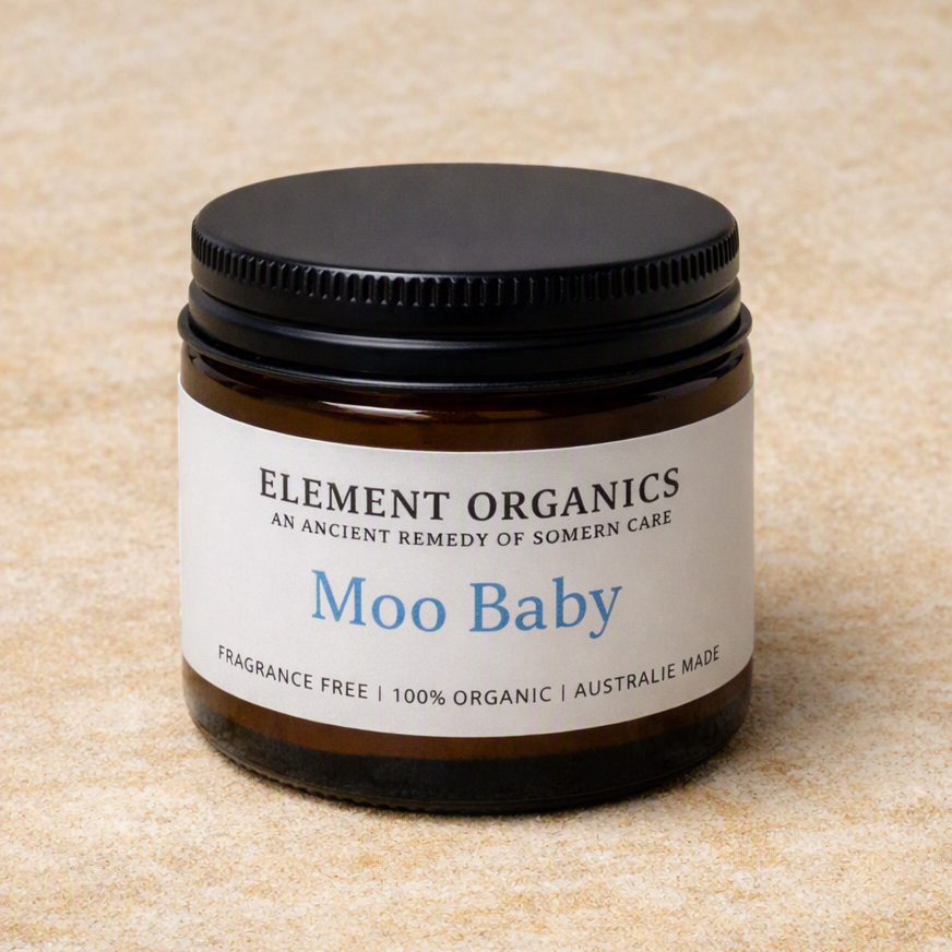 An amber glass jar candle with a black screw-on lid and a white label reading 'ELEMENT ORGANICS' and 'Moo Baby' on a beige textured background.