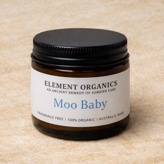 An amber glass jar candle with a black screw-on lid and a white label reading 'ELEMENT ORGANICS' and 'Moo Baby' on a beige textured background.