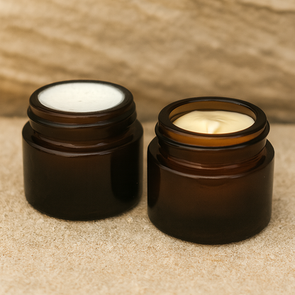 Two small amber glass jars tallow face cream and golden tallow balm inside. Jars sit on a sandstone background.